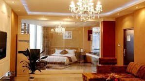 A modern hotel room with a large bed, a seating area with a sofa, a chandelier, and a television. - Li'ao Apartment Hotel (NANTONG)