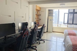 A hotel room with a desk, two chairs, a bed, and a window with blinds.
