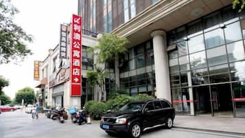 A building with a large glass facade, a red sign indicating a hotel, and a black SUV parked in front.