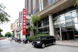 Un edificio con una grande facciata vetrata, un cartello rosso che indica un albergo e un SUV nero parcheggiato di fronte.