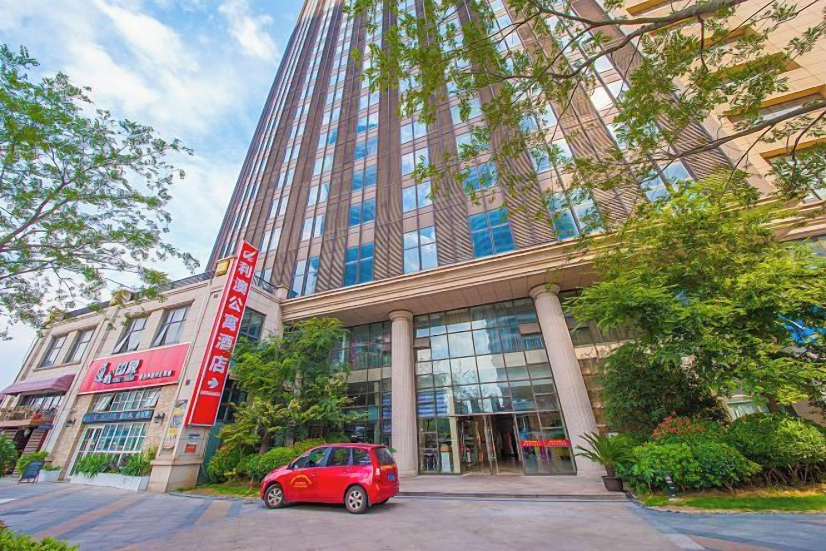 A modern building with a prominent entrance, large windows, and a red car parked in front.