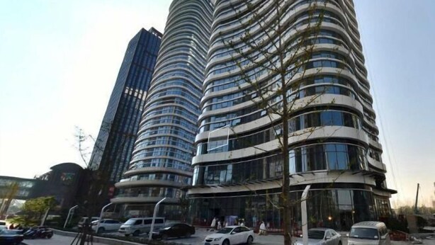 A modern high-rise building with a curved facade, large windows, and a parking area in front. - Li'ao Apartment Hotel (NANTONG)