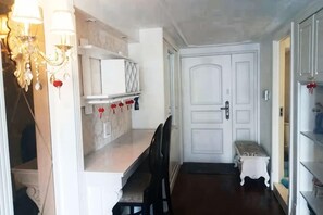 Un couloir avec une porte blanche, un banc et une étagère sur laquelle sont posés des objets rouges.