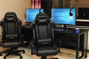 Deux fauteuils de jeu noirs, un bureau avec un ordinateur et deux écrans.