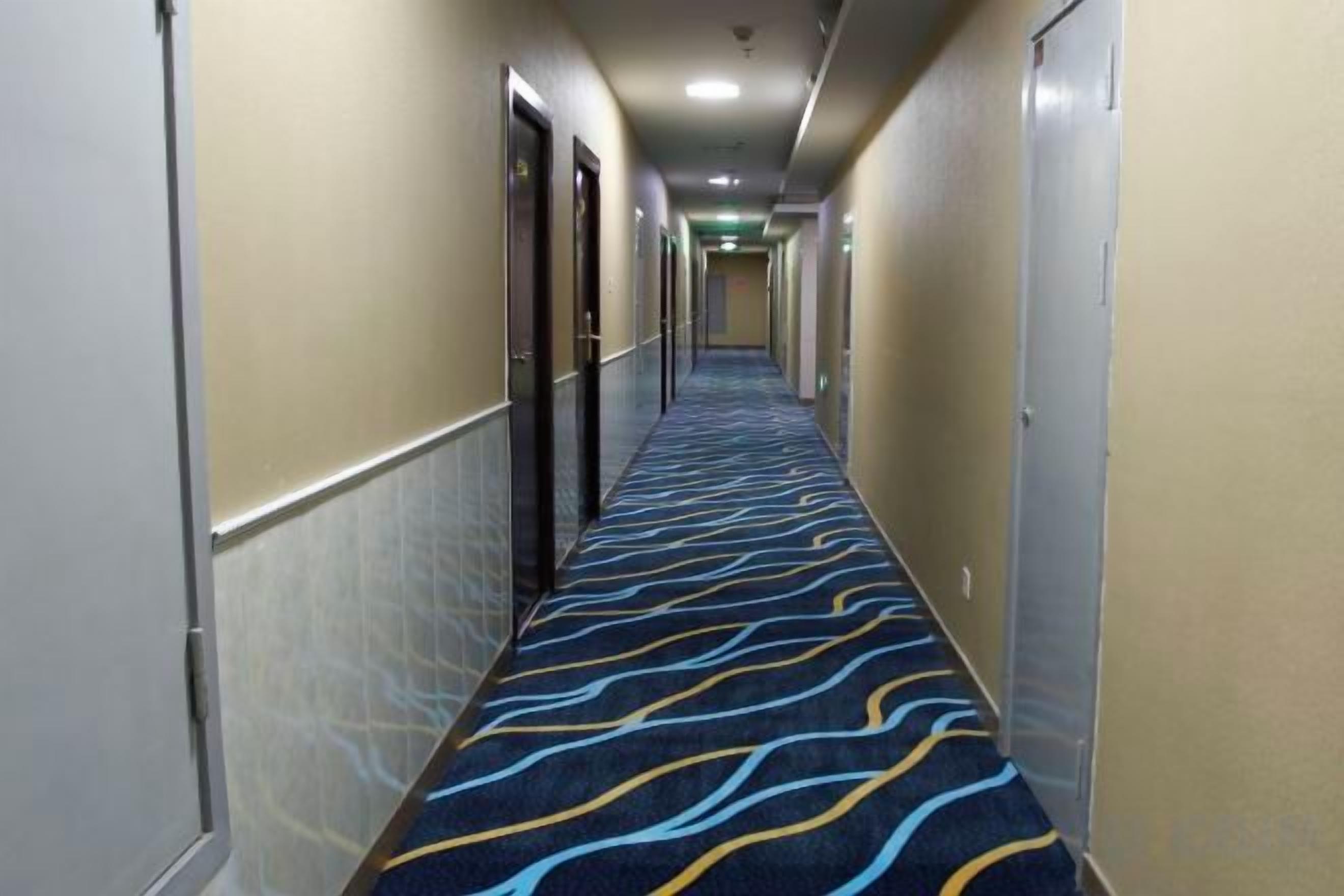 A hotel corridor with a patterned carpet, doors, and a light fixture on the ceiling.