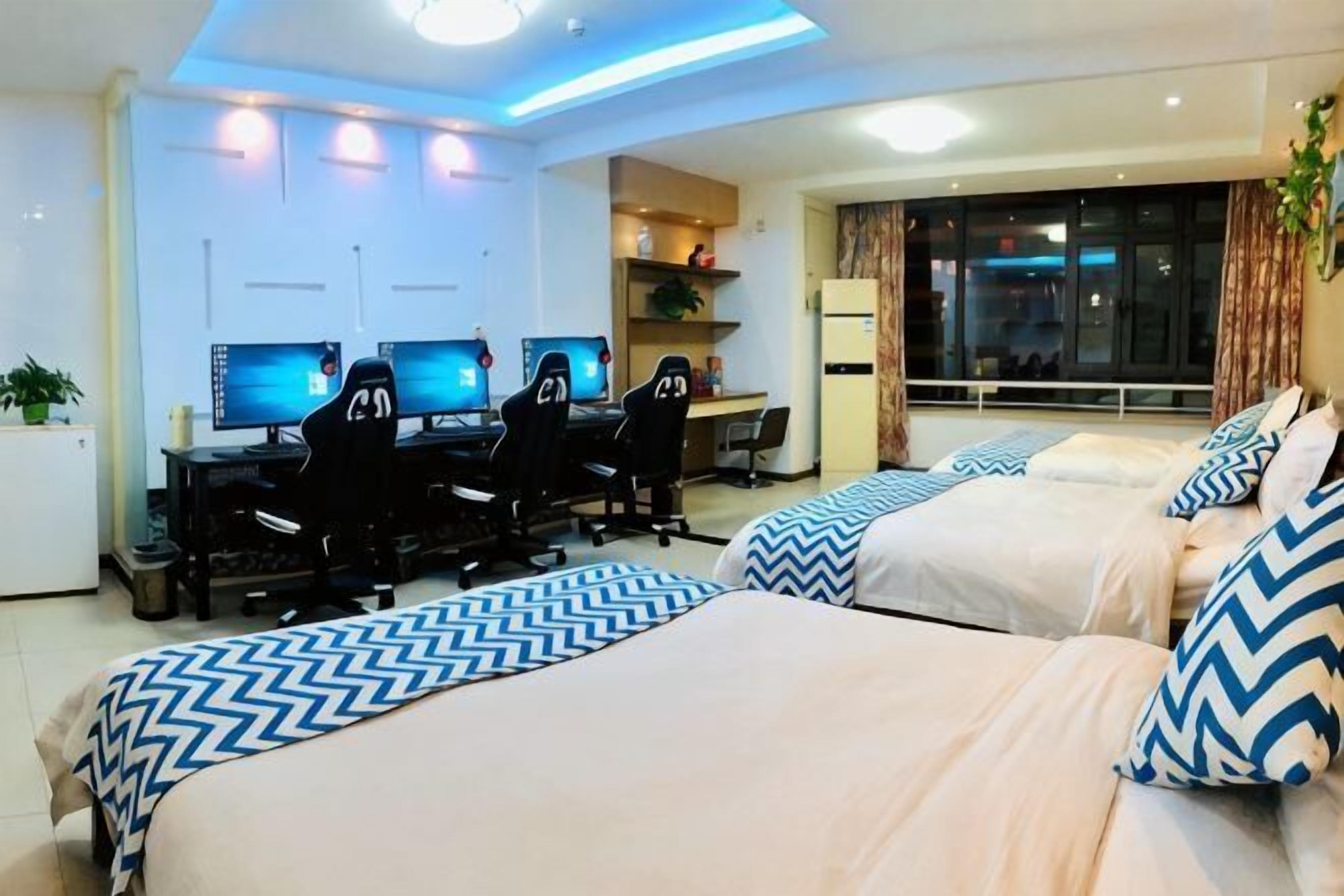 Ein Hotelzimmer mit zwei Betten, einem Schreibtisch mit Computern und einem großen Fenster.