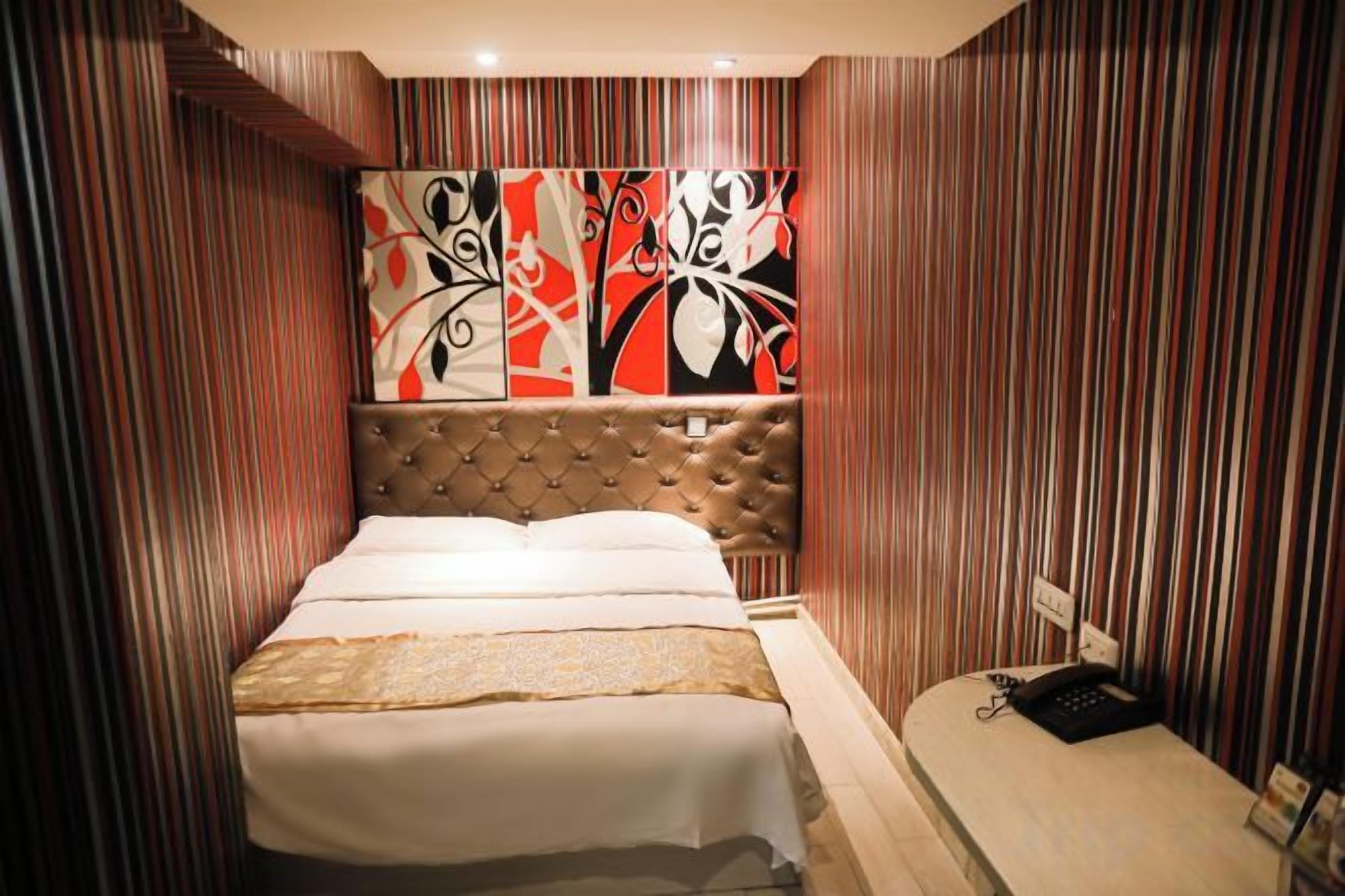 Habitación de hotel con cama, cabecero, mesita de noche y pared con rayas verticales.