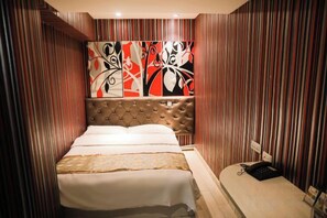A hotel room with a bed, a headboard, a bedside table, and a wall with vertical stripes.