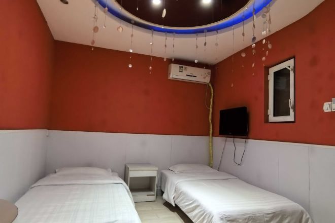A room with two beds, an air conditioning unit, a TV mounted on the wall, and a ceiling with hanging lights.