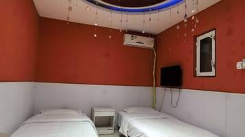A room with two beds, an air conditioning unit, a TV mounted on the wall, and a ceiling with hanging lights.