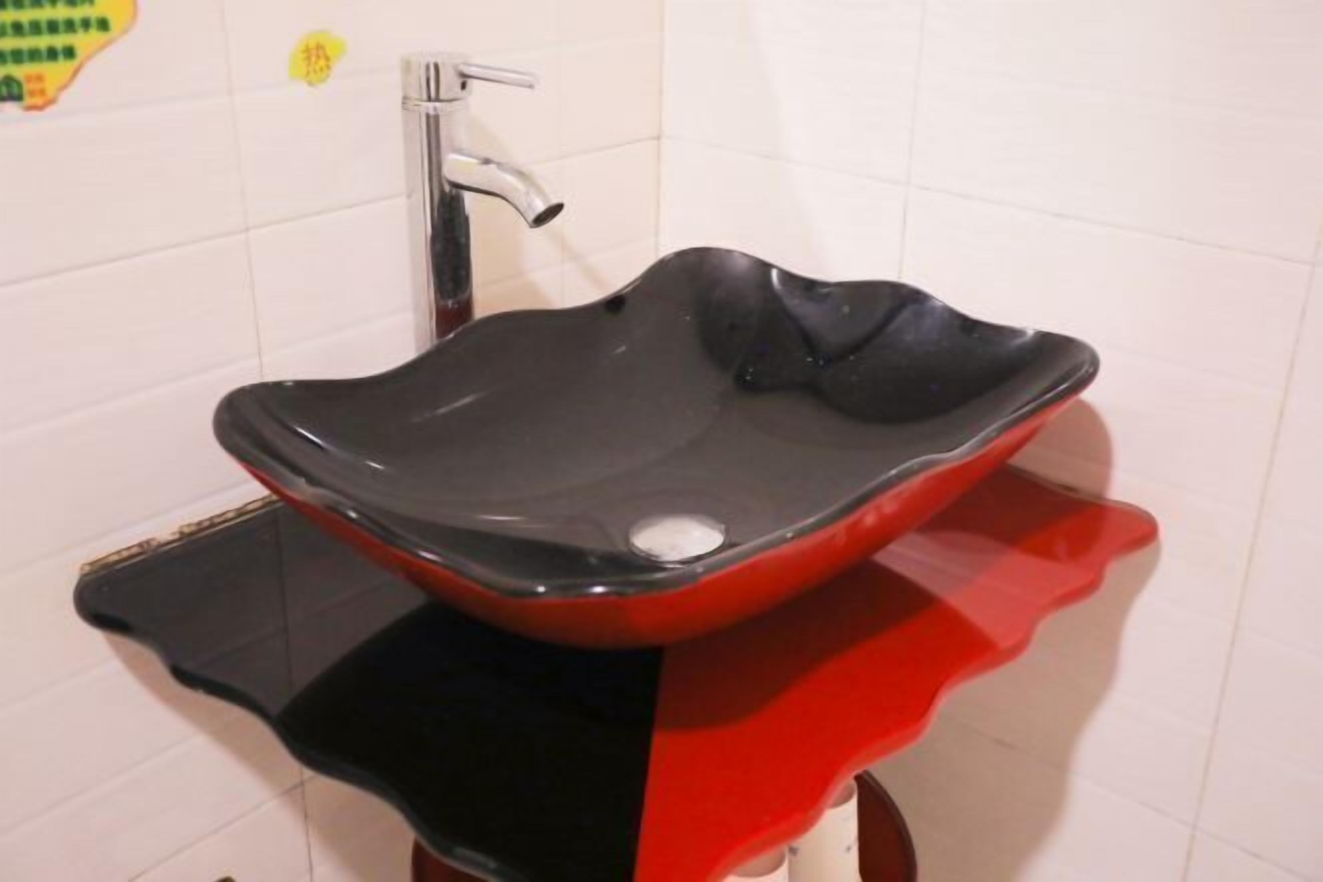 A bathroom with a black and red glass sink, a chrome faucet, and white tiled walls.