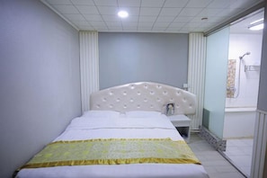 A bedroom with a bed, bedside table, and a shower area.