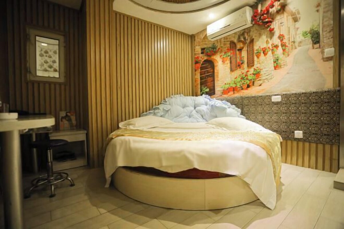 A room with a round bed, a small desk, and a wall mural.