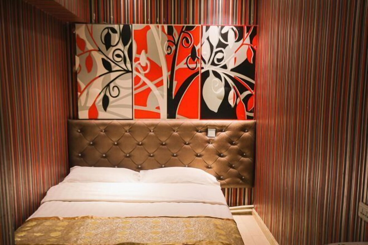 A bedroom with a tufted headboard, a bed with white linens, and a striped wall with abstract art.