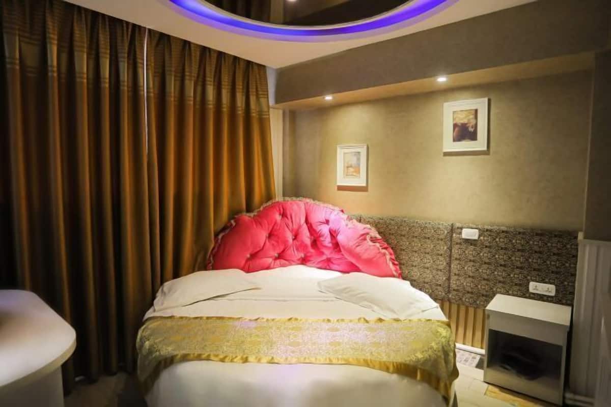 Une chambre d’hôtel avec un lit, des rideaux, une tête de lit et deux tableaux encadrés accrochés au mur.
