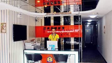Un área de recepción con un escritorio, sillas, una computadora y un gran cartel rojo con texto.