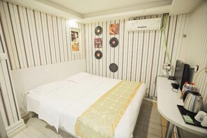 A hotel room with a bed, a desk, an air conditioner, and wall decorations including vinyl records.