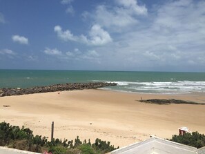 A beach with a rocky breakwater, clear skies, and calm sea. - Hotel Paraiso Natal (Natal)