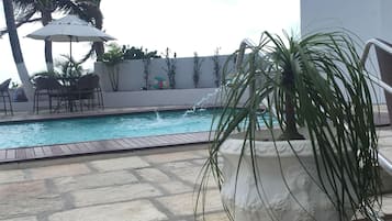 Área de piscina com piso de pedra, um vaso branco com uma planta e um mural na parede.