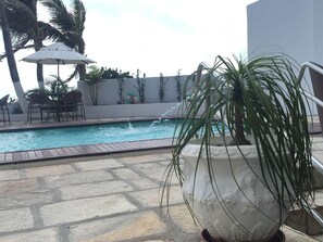 A pool area with a stone floor, a white planter with a plant, and a mural on the wall.