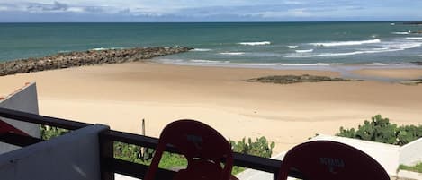 A beach view from a balcony with two red chairs labeled 'DEVASSA'.
