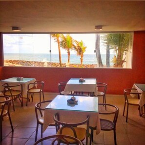 A restaurant with tables and chairs, a view of the beach, and palm trees. - Hotel Paraiso Natal (Natal)