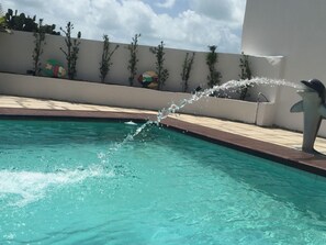 A swimming pool with a dolphin statue and water jets. - Hotel Paraiso Natal (Natal)
