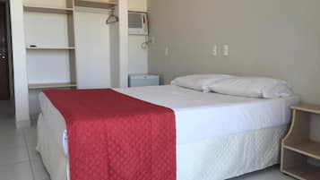 Un dormitorio con cama, manta roja, almohada blanca, mesita de noche y armario.