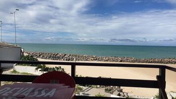 Vista da praia a partir de uma varanda com uma mesa identificada como 'DEVASSA'.