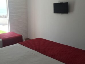 A room with two beds, one with a red bedspread and the other with a white bedspread. There is a black object on the wall, possibly a speaker or a small screen.