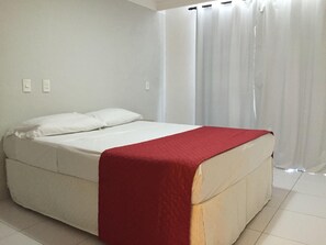 A single-bed room with a white mattress, a red blanket, and white curtains. - Hotel Paraiso Natal (Natal)