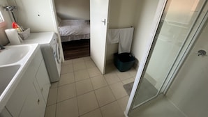 A compact bathroom with a washing machine, a bed, and a shower area.
