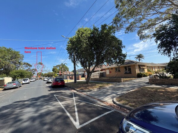 A street with cars parked on the side, a clear sky, and a building with a sign that reads "Mentone train station".