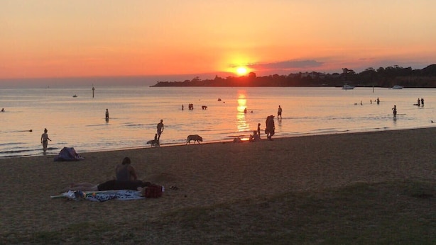 A beach at sunset with people and boats.