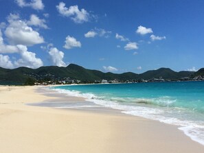 A beach with clear turquoise waters, a sandy shore, and a backdrop of green hills.