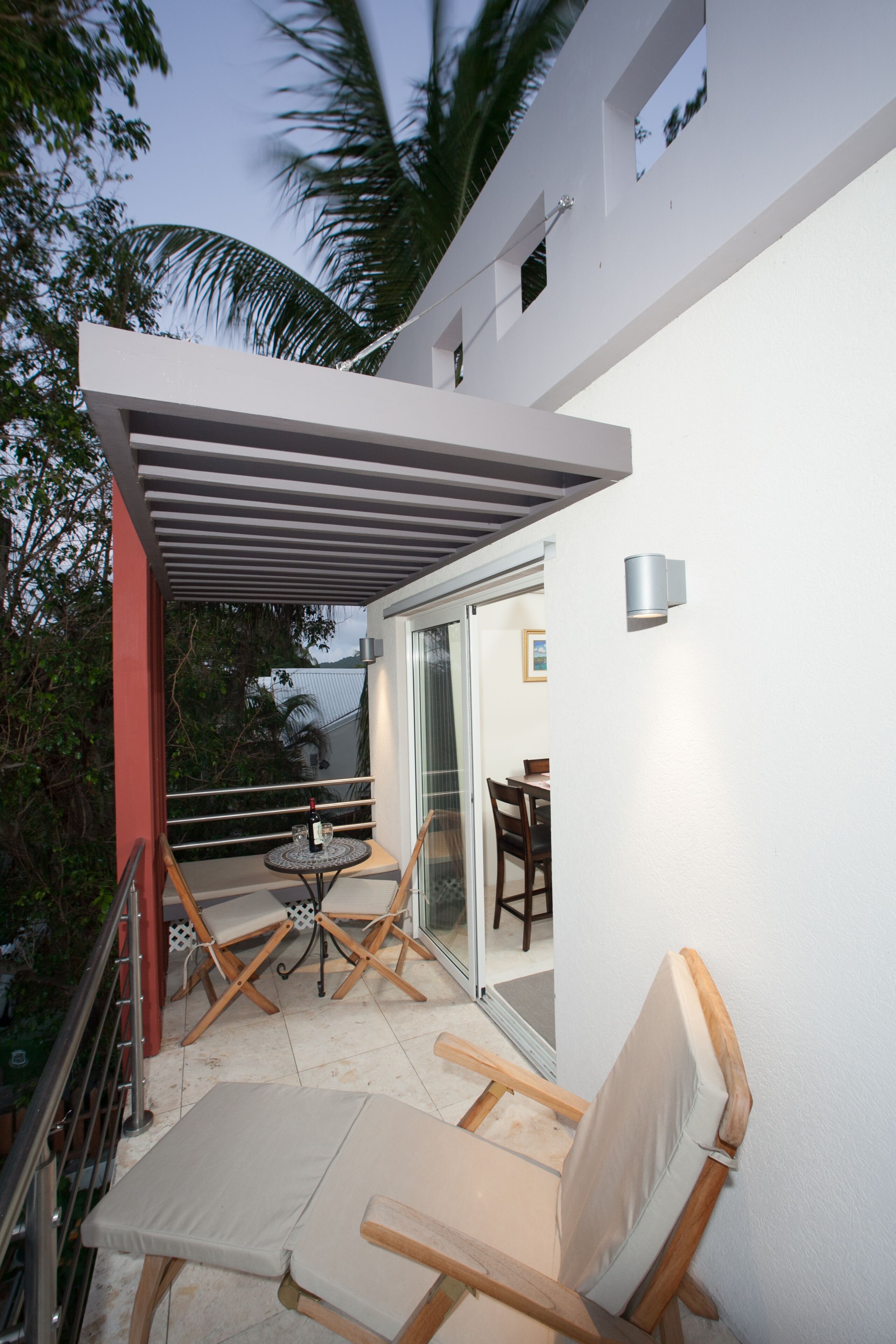 Une terrasse extérieure moderne, dotée d’une table et de chaises, d’une pergola et d’une porte vitrée donnant sur un espace intérieur.