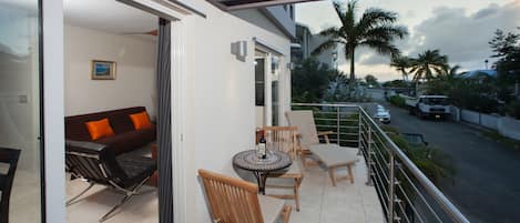 A balcony with a table and chairs, a sofa, and a view of the street and palm trees.