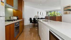 A modern kitchen with wooden cabinets, a white countertop, and a dining area with chairs and a table.