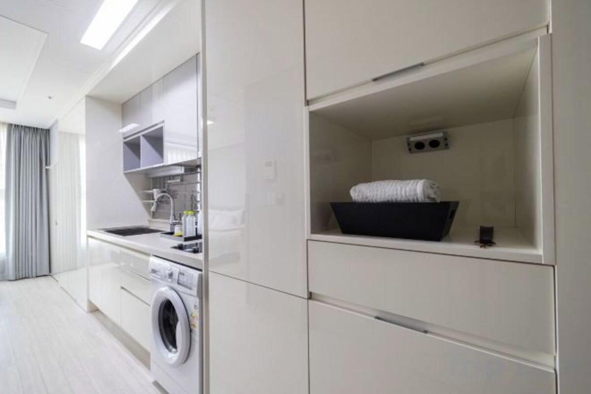 A modern kitchen with built-in appliances, a washing machine, and a black storage bin on a shelf.