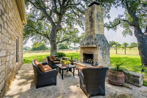 An outdoor patio with wicker furniture, a stone fireplace, and a view of a grassy field. - Secluded Farmhouse, vineyard on 4 acres, near wineries, shaded yard & EV charger (Fredericksburg)