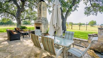Relax in a serene outdoor space with a fireplace, comfortable seating, and a lush green view.