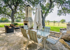 Eine Terrasse im Freien mit Steinböden, Korbmöbeln, einem Glastisch, gestreiften Stühlen und einem Kamin aus Stein mit Schornstein.
