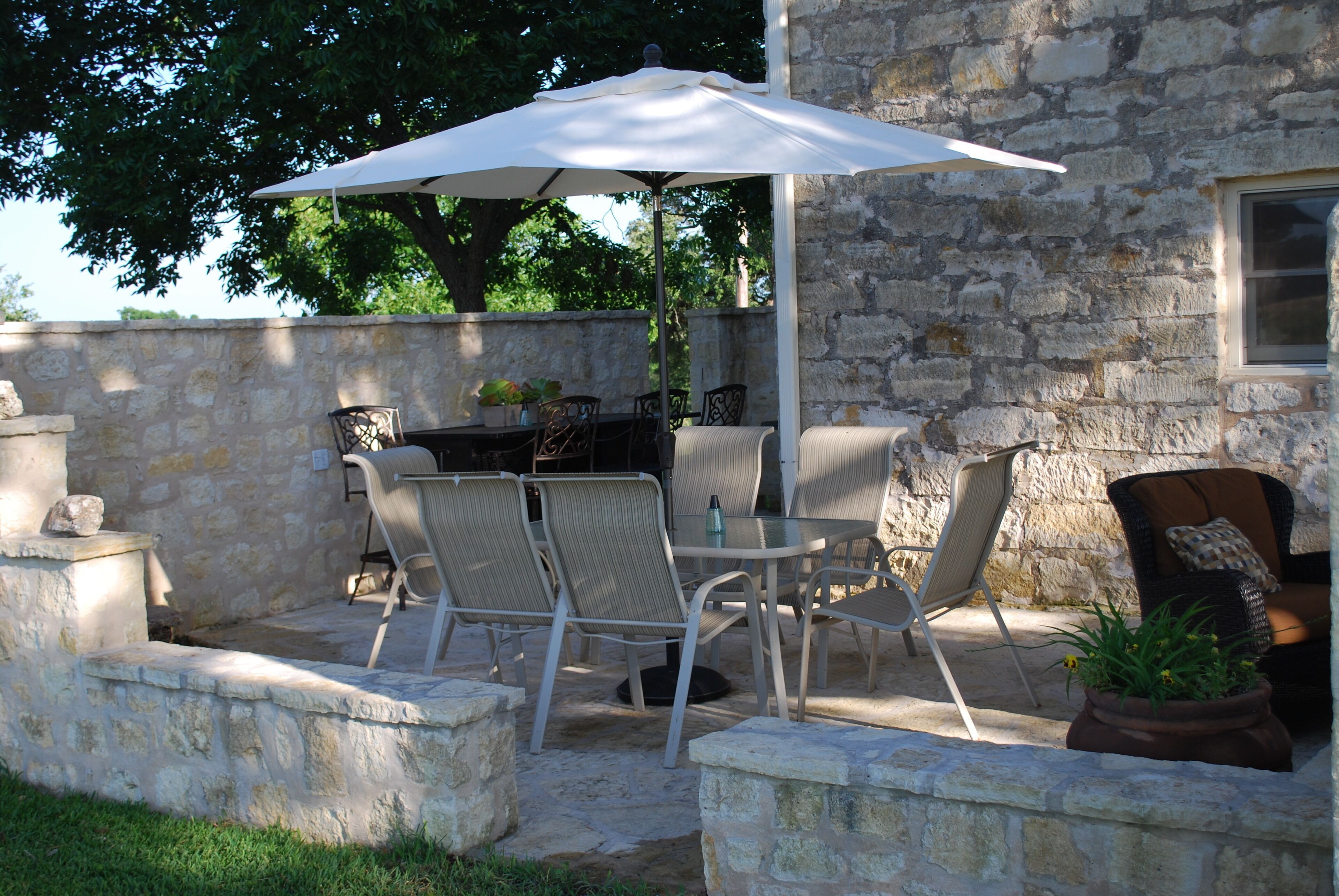 Een terras buiten met stenen muren, een tafel met stoelen en een grote parasol.