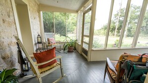 Une véranda avec un fauteuil à bascule, un fauteuil roulant et une vue sur le jardin.