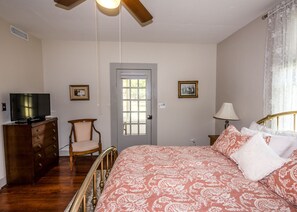 Ein Schlafzimmer mit einem Bett, einem Fernseher auf einer Kommode, einem Sessel, einer Tür und einer Lampe.