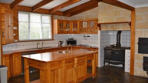 A kitchen with wooden cabinets, a large island, a stone wall, and a wood-burning stove. - The luxury guest house Busselton (Busselton)