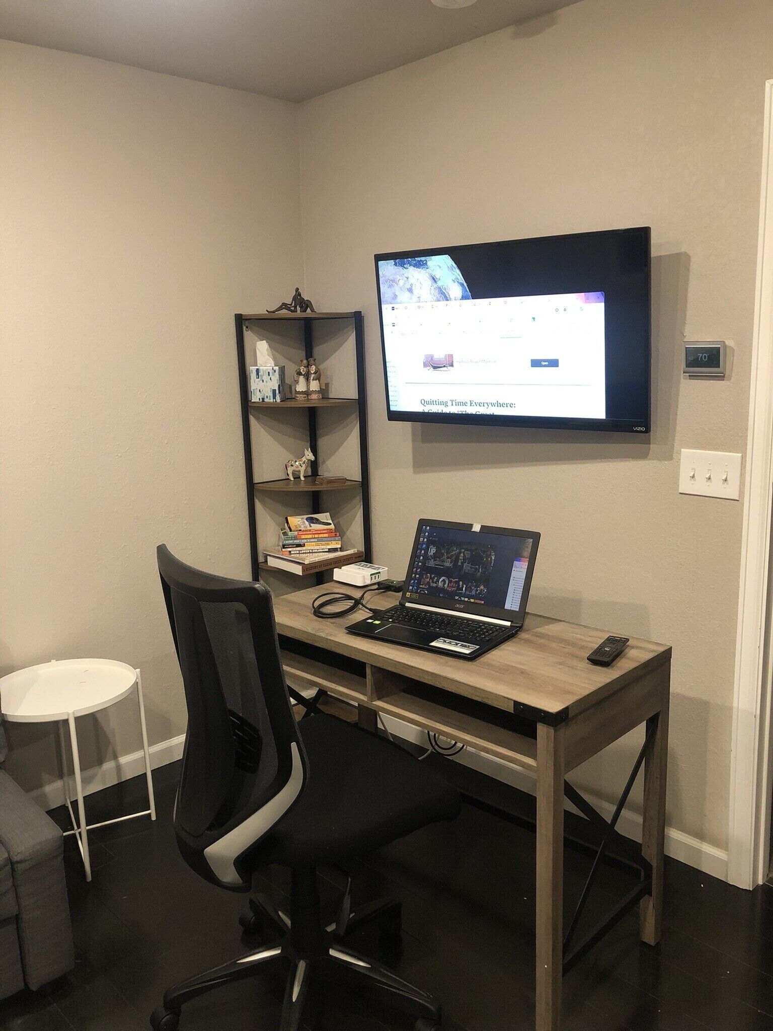 A workspace with a desk, chair, laptop, and a TV mounted on the wall.
