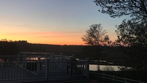 Avarakatoksen kaltainen rakennelma, jossa on kaide, ja josta avautuu näkymä vesistöön auringonlaskun aikaan.
