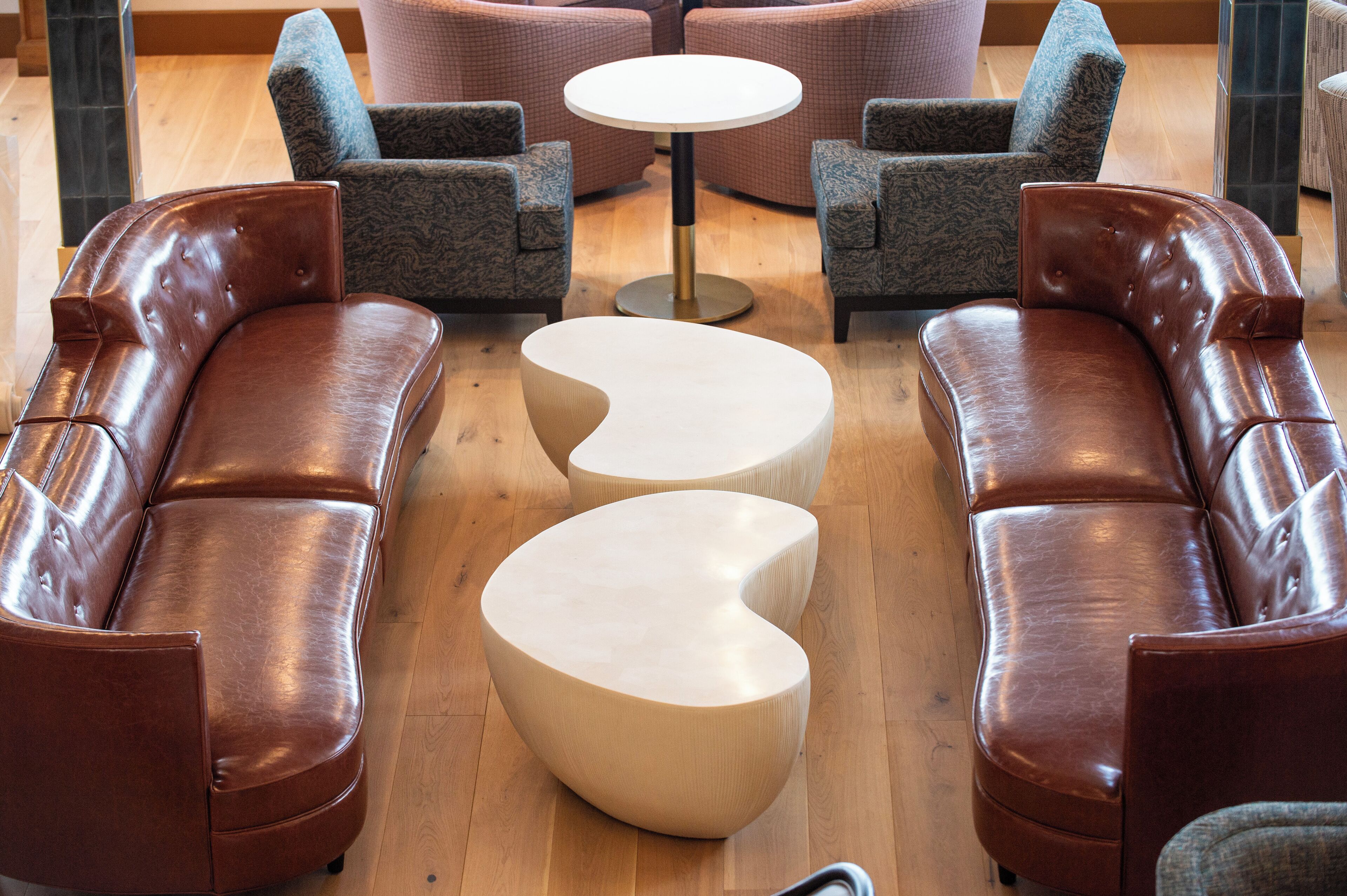 A modern lounge area with leather sofas, patterned armchairs, and a central round table.