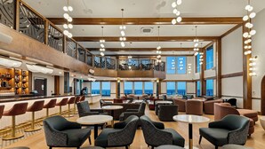 A spacious lounge area with multiple seating options, a bar, and large windows offering a view of the sea.